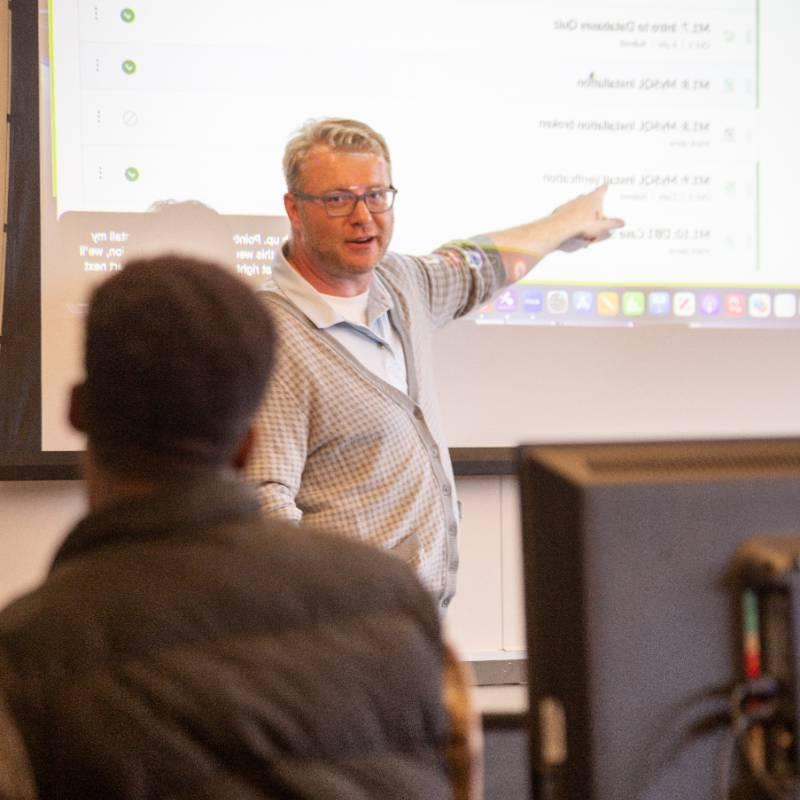 a professor pointing to a screen in a classroom